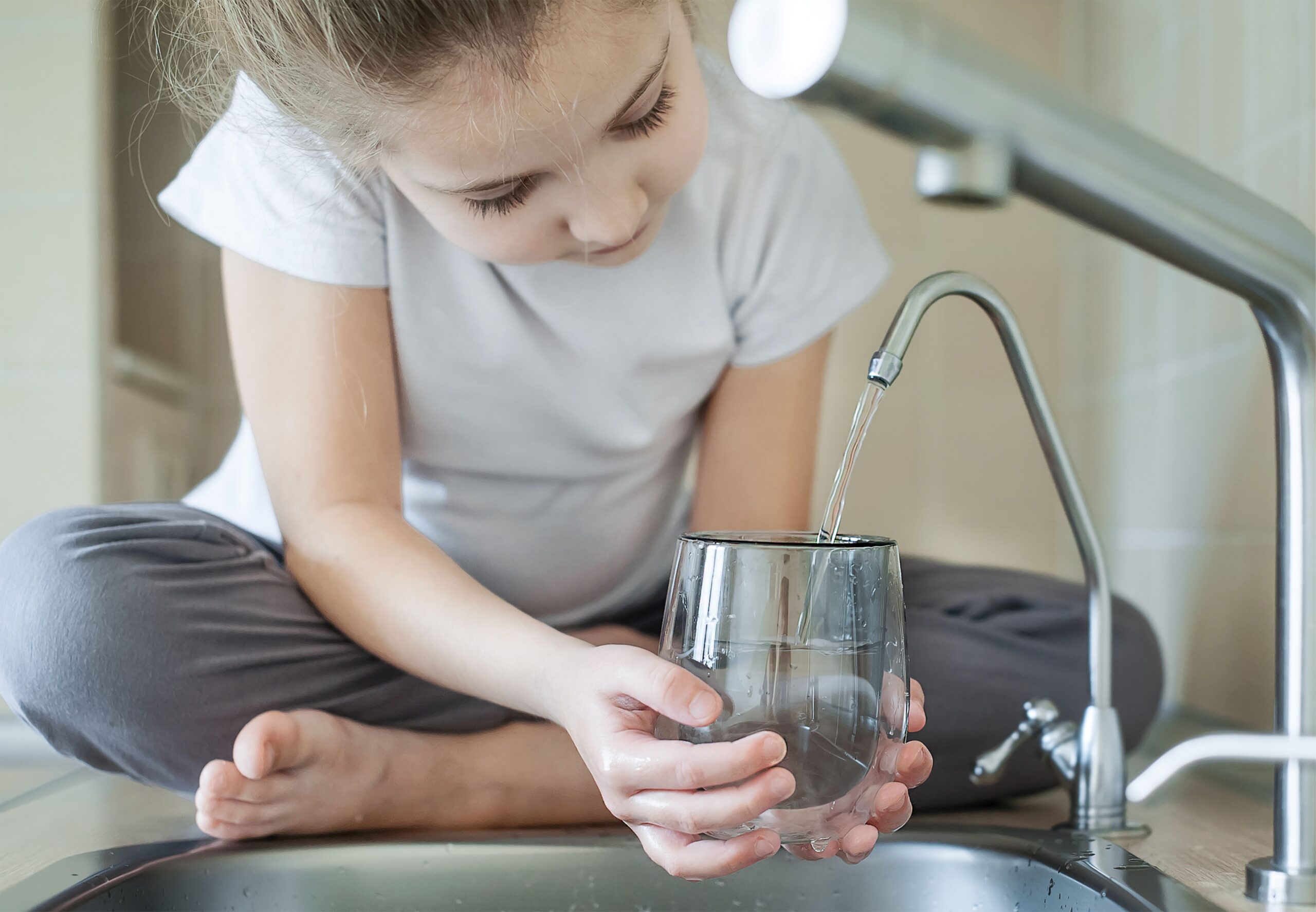 Kind füllt ein Glas an Osmose Wasserfilter-Armatur – sauberes Trinkwasser dank moderner Küchentechnologie