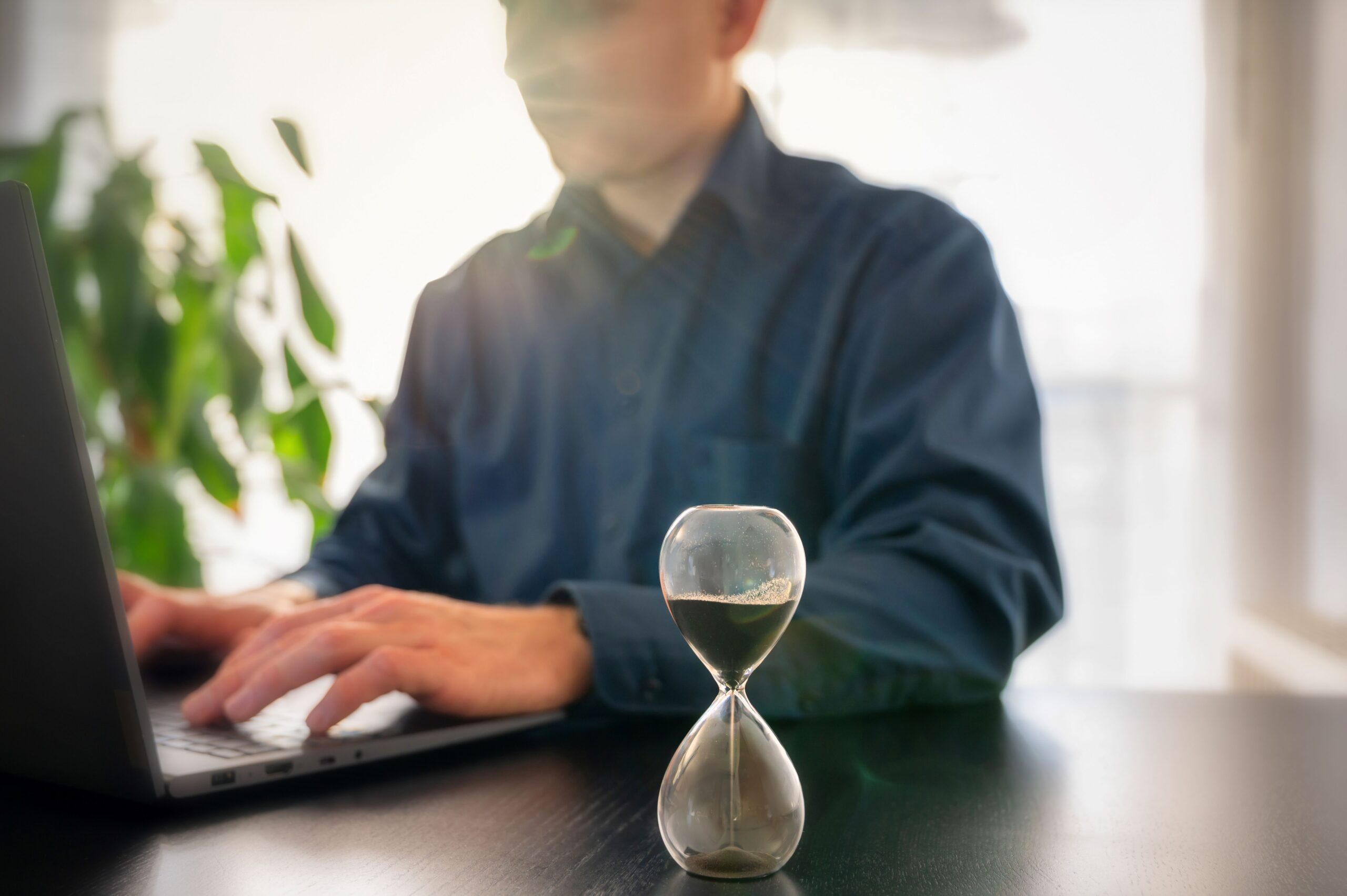 Eine Sanduhr steht vor jemandem der am PC arbeitet