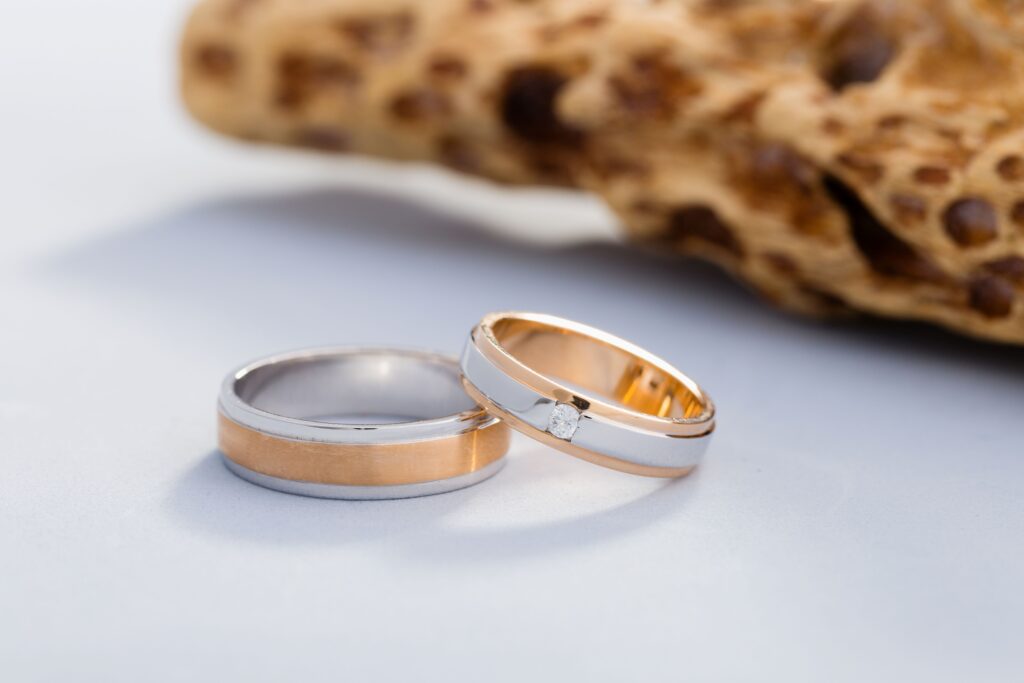 Zwei Trauringe in Gold-Weiß-Optik mit Diamant auf hellem Hintergrund neben Naturstein