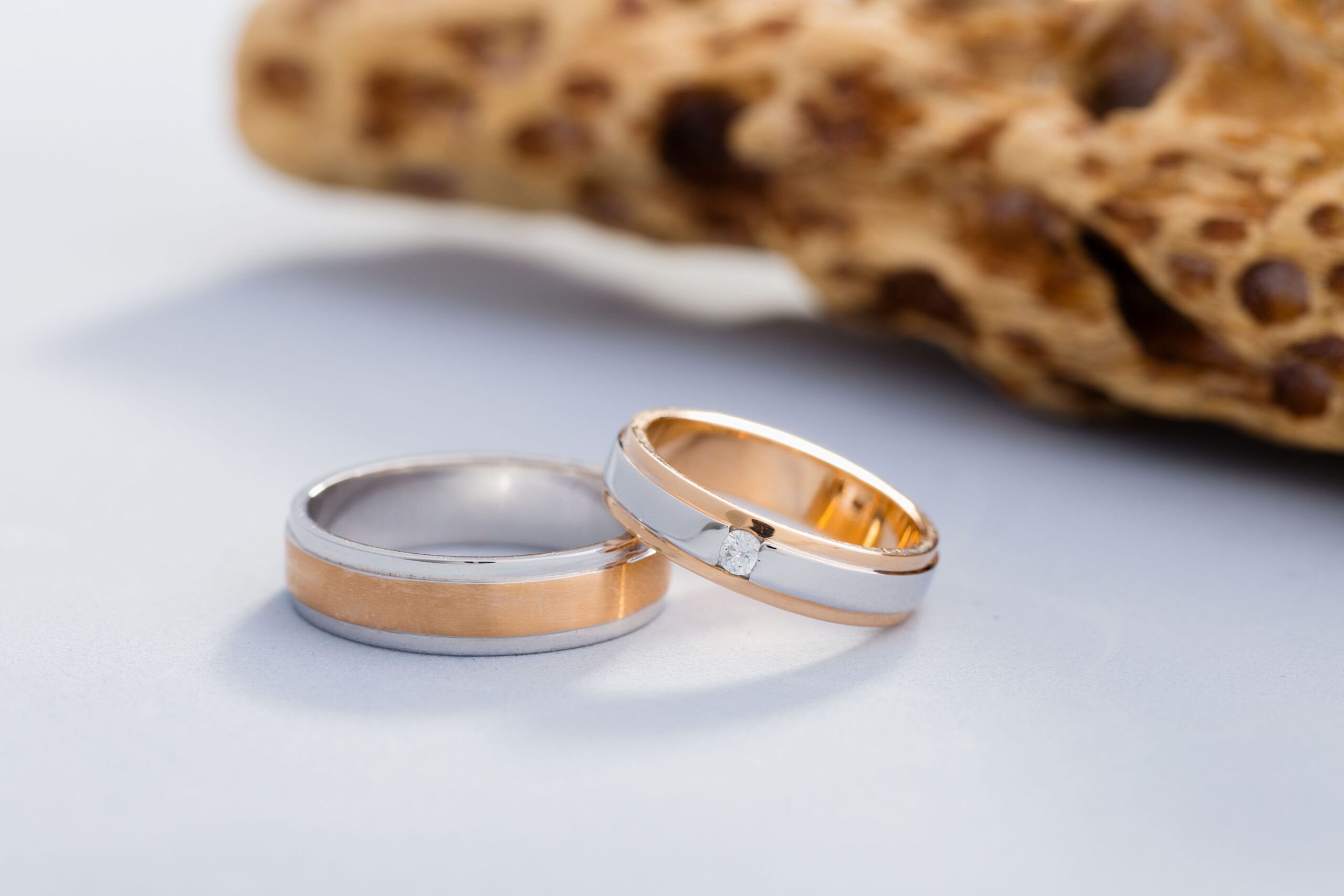 Zwei Trauringe in Gold-Weiß-Optik mit Diamant auf hellem Hintergrund neben Naturstein